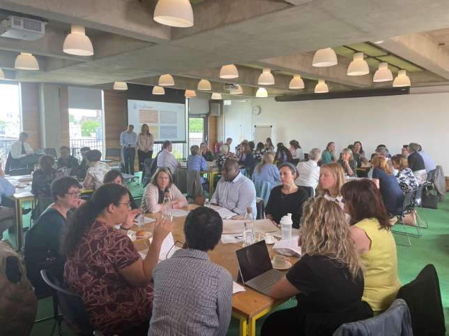 Large room filled with people sitting ten to a desk at an event